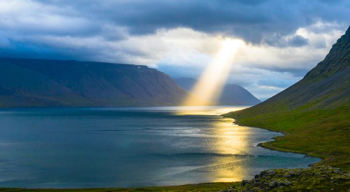 un valle con agua y del cielo sale un rayo de sol