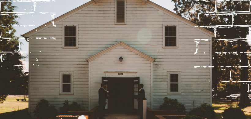 una iglesia de madera blanca con dos hombres afuera