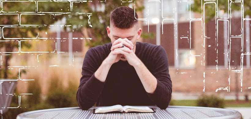 un hombre orando con una biblia alfrente de el