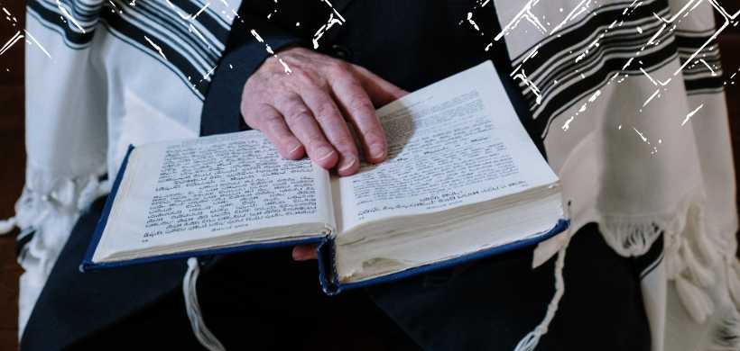 un hombre con un talit, sentado, leyendo una biblia