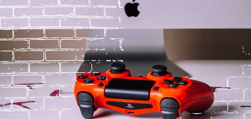 un control anaranjado de playstation cerca de una computadora de apple